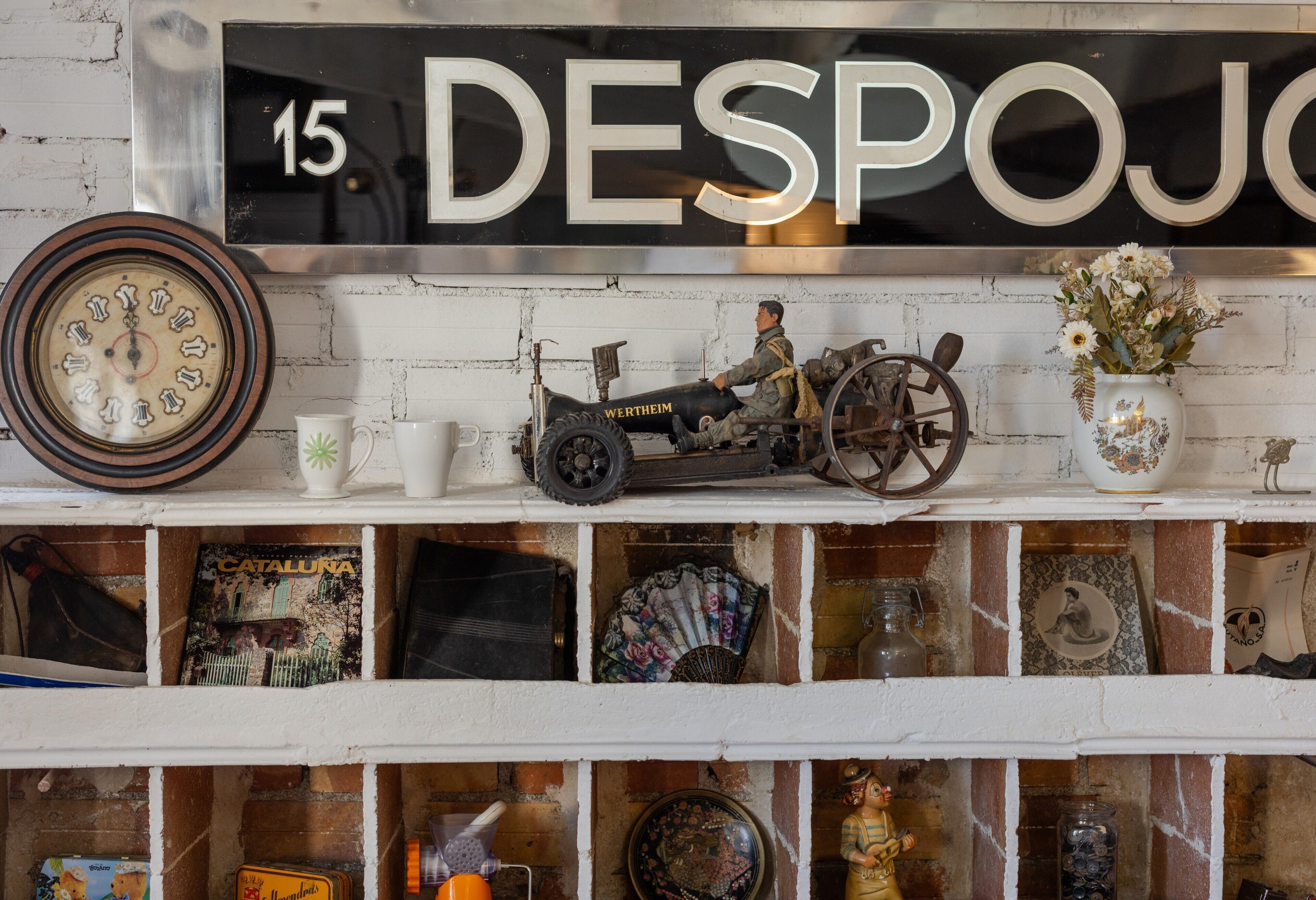 Una estantería con objetos antiguos, incluyendo un coche modelo, un reloj y platos decorativos.