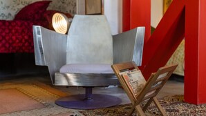 A modern room with a metallic chair, a red accent wall, and a small wooden easel with a magazine.