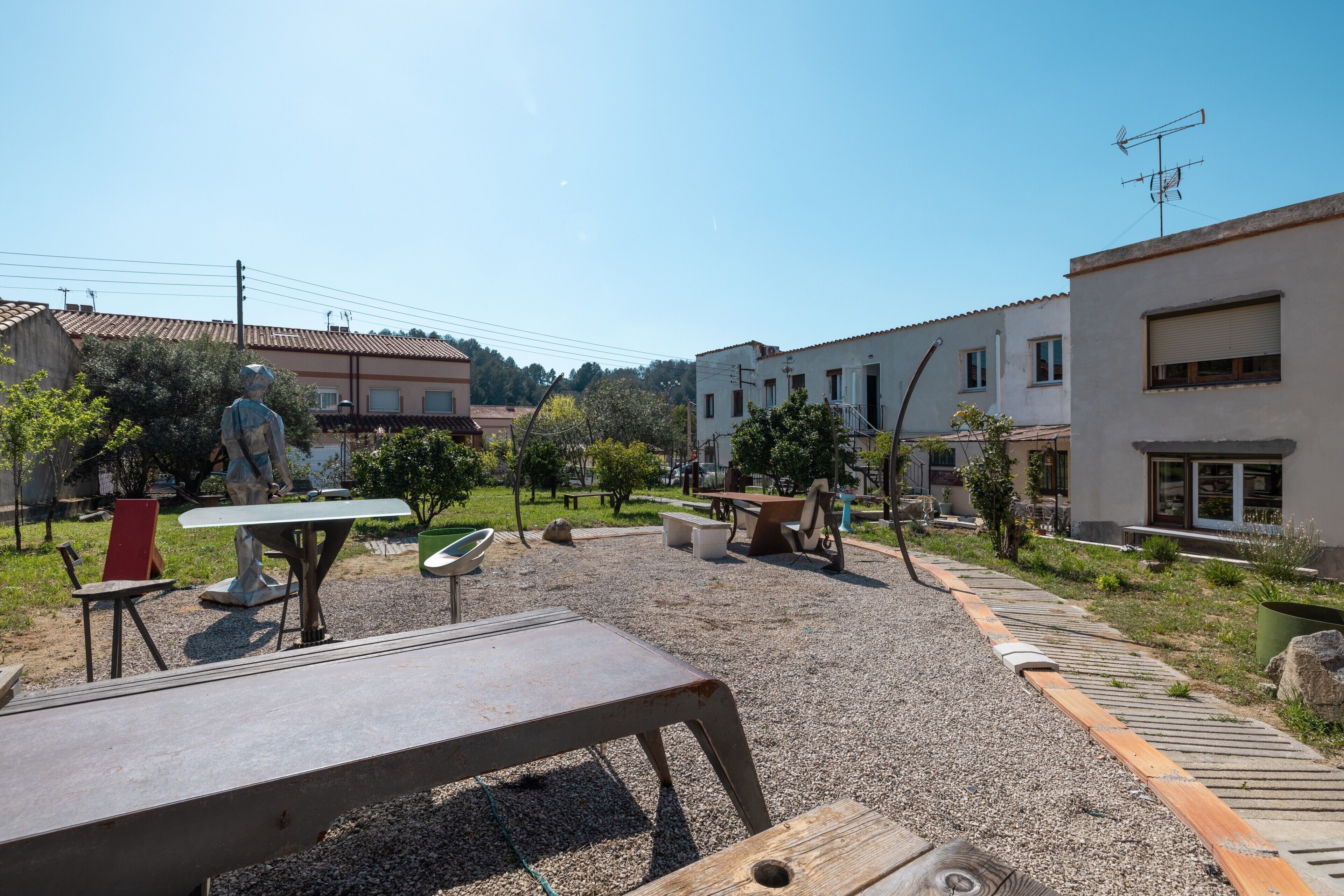 Un espacio al aire libre con una mesa y sillas, una escultura y un edificio con ventanas y un balcón.