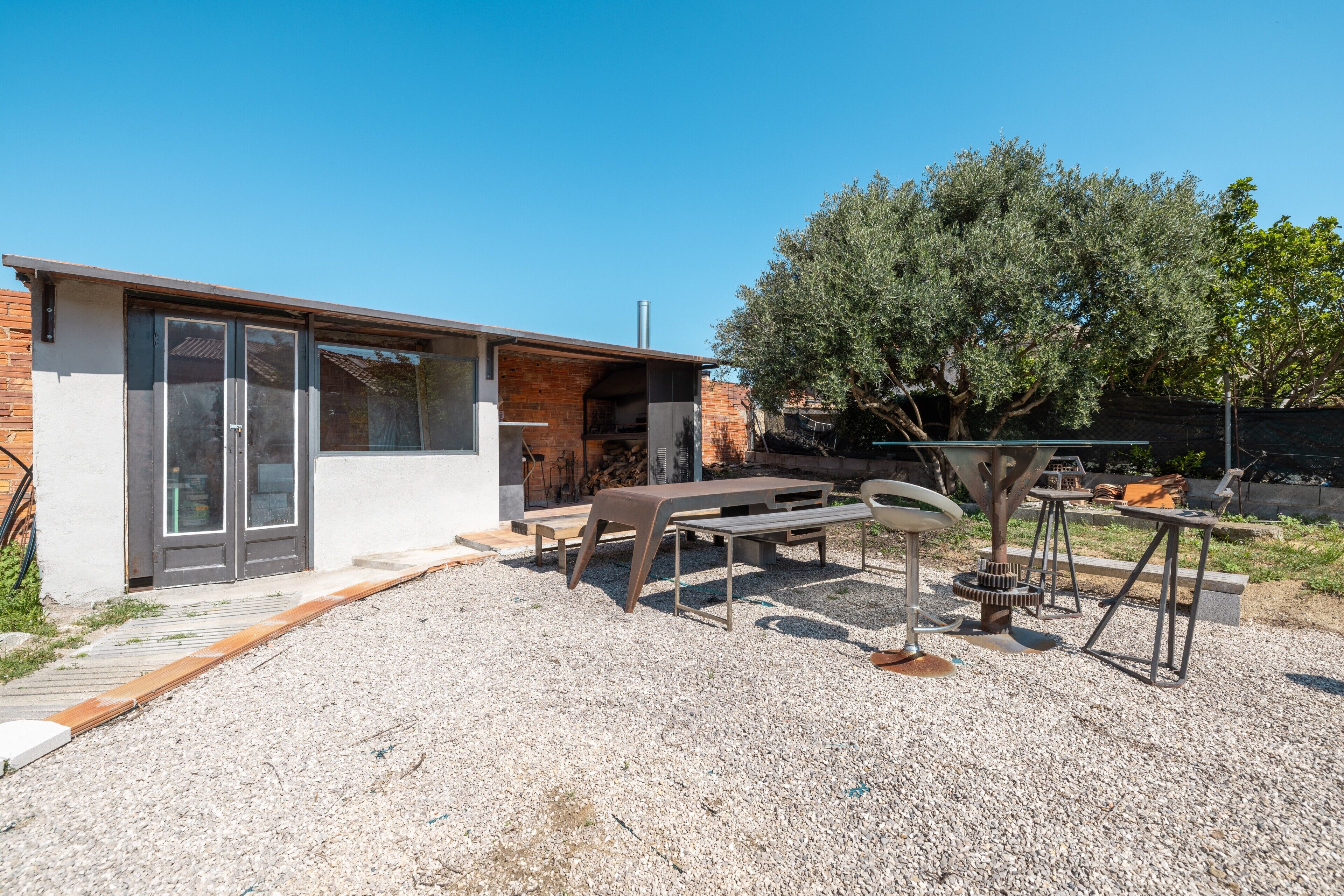 A modern outdoor patio with a brick building, a table, chairs, and a pergola.