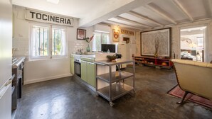 Een keuken met een bord waarop 'TOCINERIA' staat, een kar en een eetgedeelte met een rode plank.