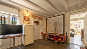 Een kamer met een televisie, een deur waarop 'ENTRADA' staat, een boekenkast en een groot abstract schilderij.