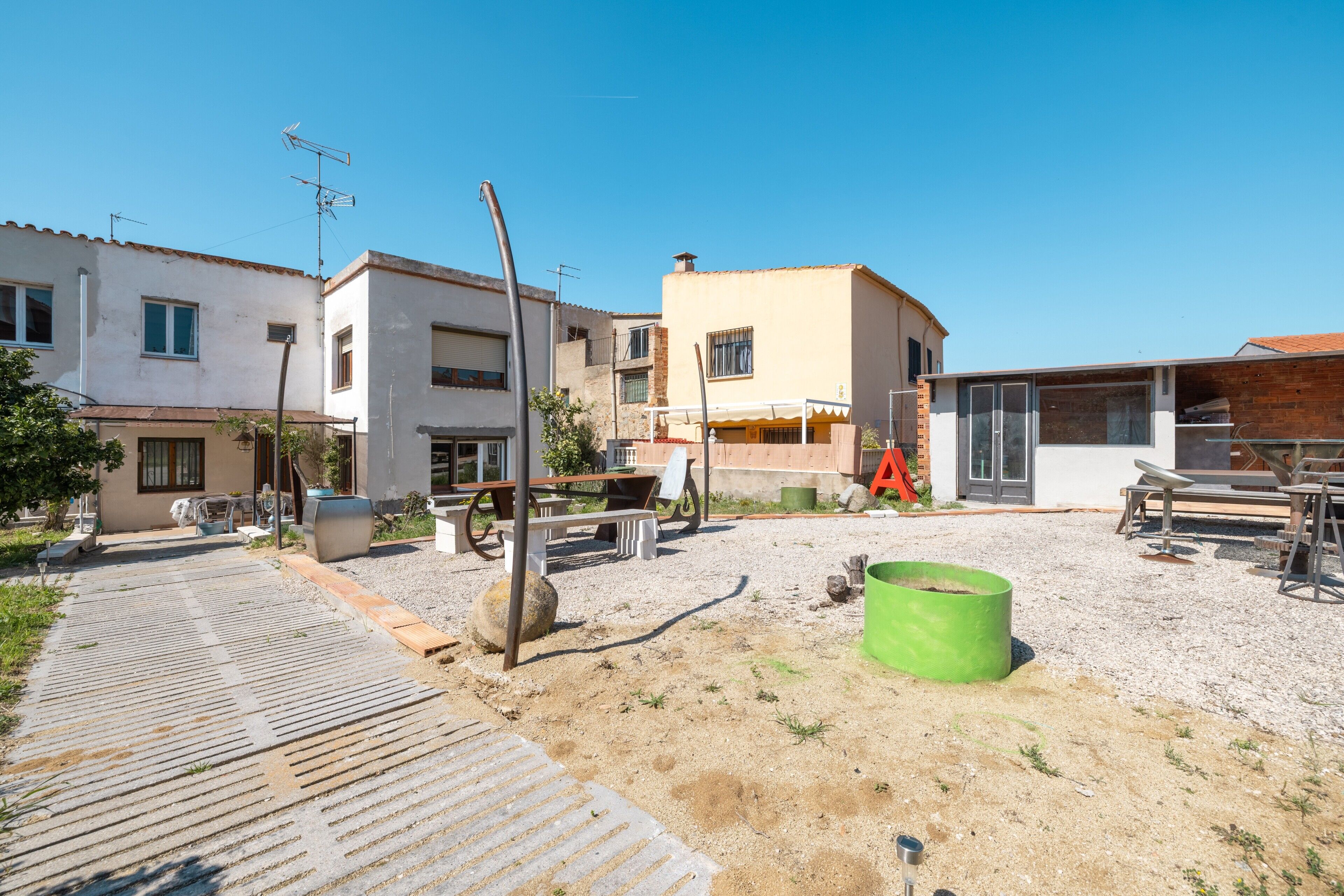 A residential area with houses, a gravel driveway, and outdoor furniture.