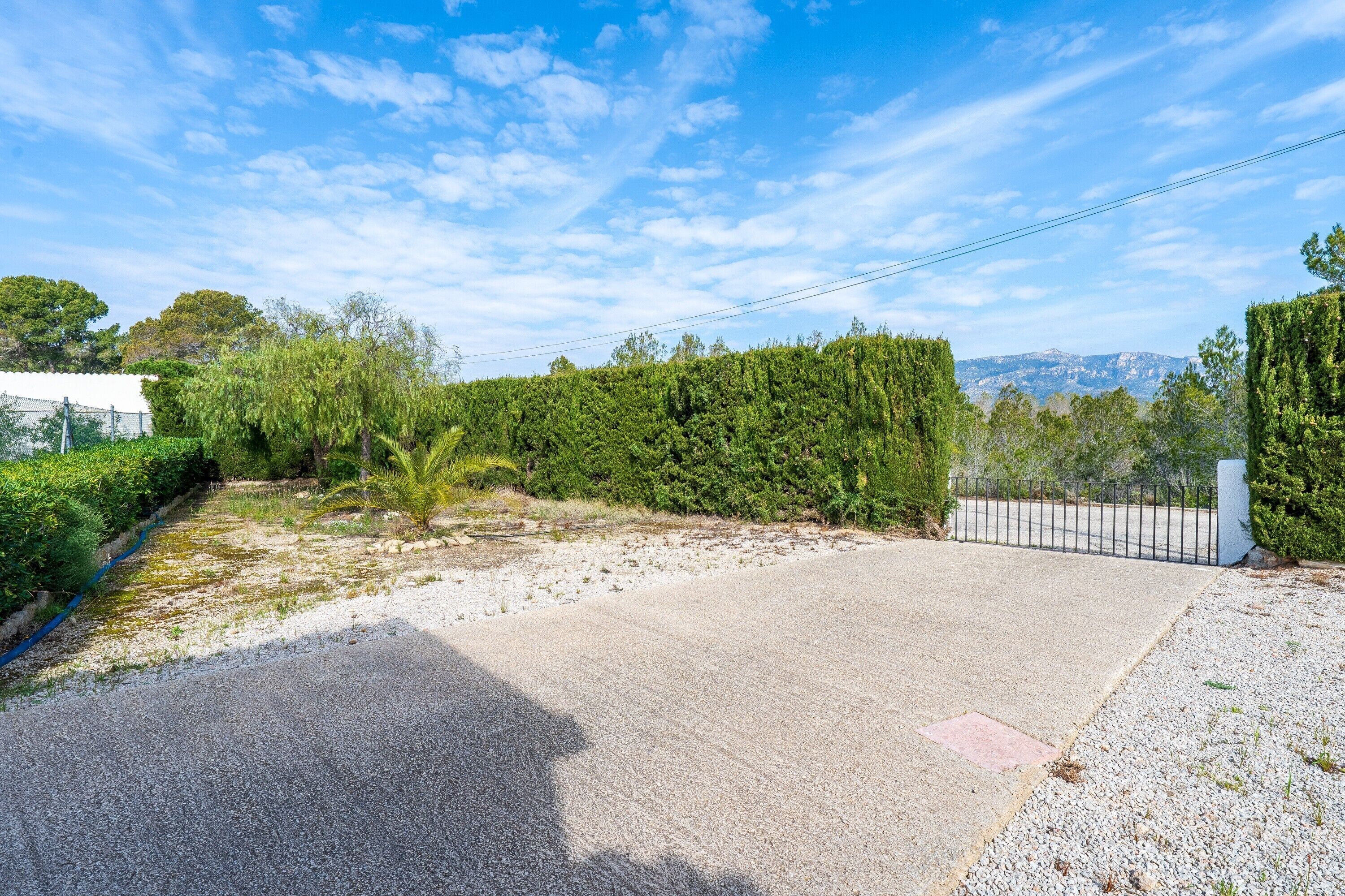 Un camino pavimentado que conduce a una zona vallada, con vistas a colinas distantes.