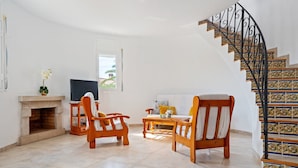 A living room with a fireplace, wooden furniture, a TV, and a staircase with decorative tiles. - Villa 'Flor' with sea views, private pool and Wi-Fi (Les Tres Cales)