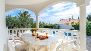 A covered outdoor dining area with a table set for breakfast, including croissants and orange juice, surrounded by white chairs. - Villa 'Flor' with sea views, private pool and Wi-Fi (Les Tres Cales)