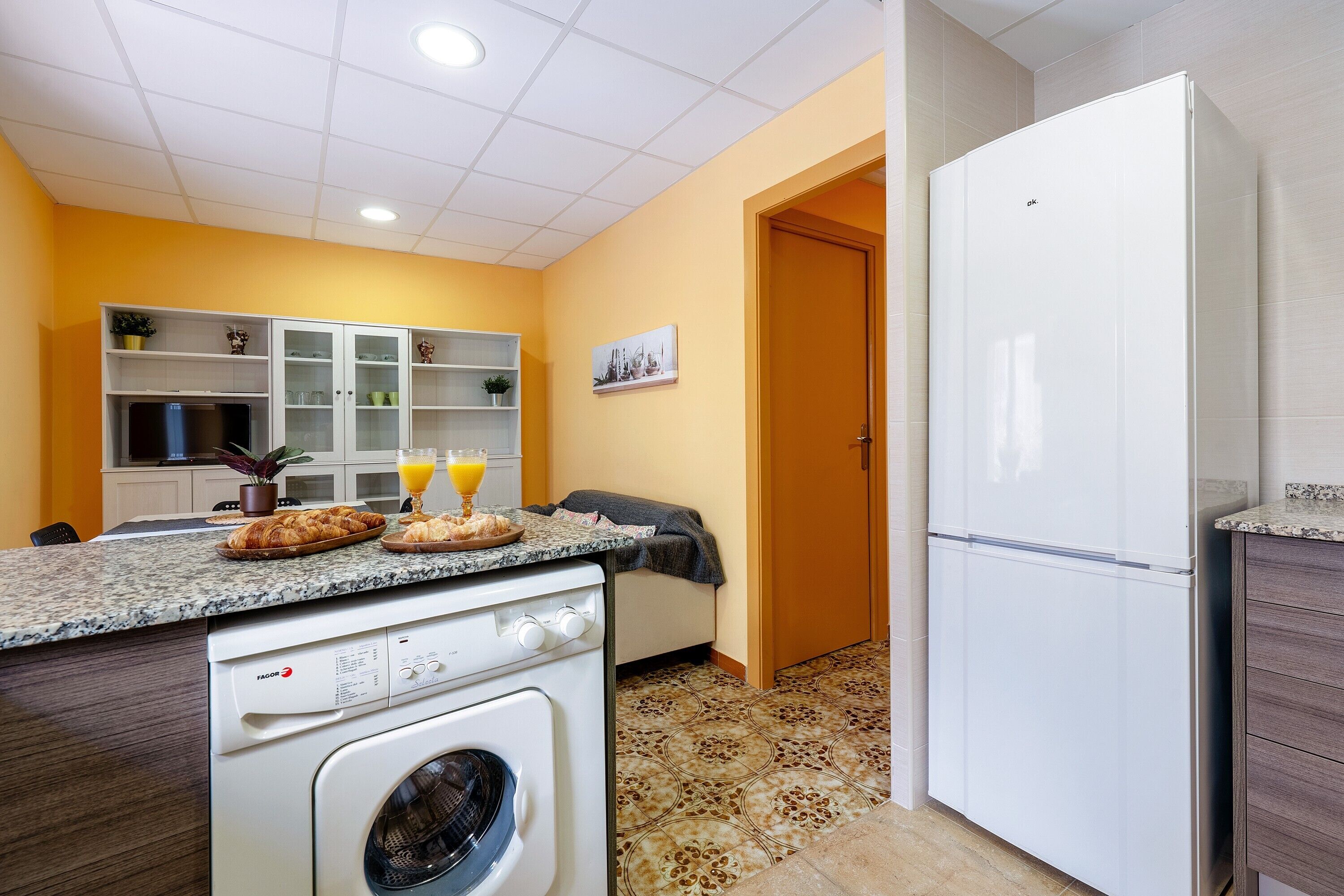 Une cuisine compacte équipée d’un lave-linge, d’un réfrigérateur et d’un coin repas avec une table mise pour le petit-déjeuner.
