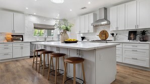 Een moderne keuken met witte kasten, een groot eiland met krukken, een gasfornuis en een raam met uitzicht.