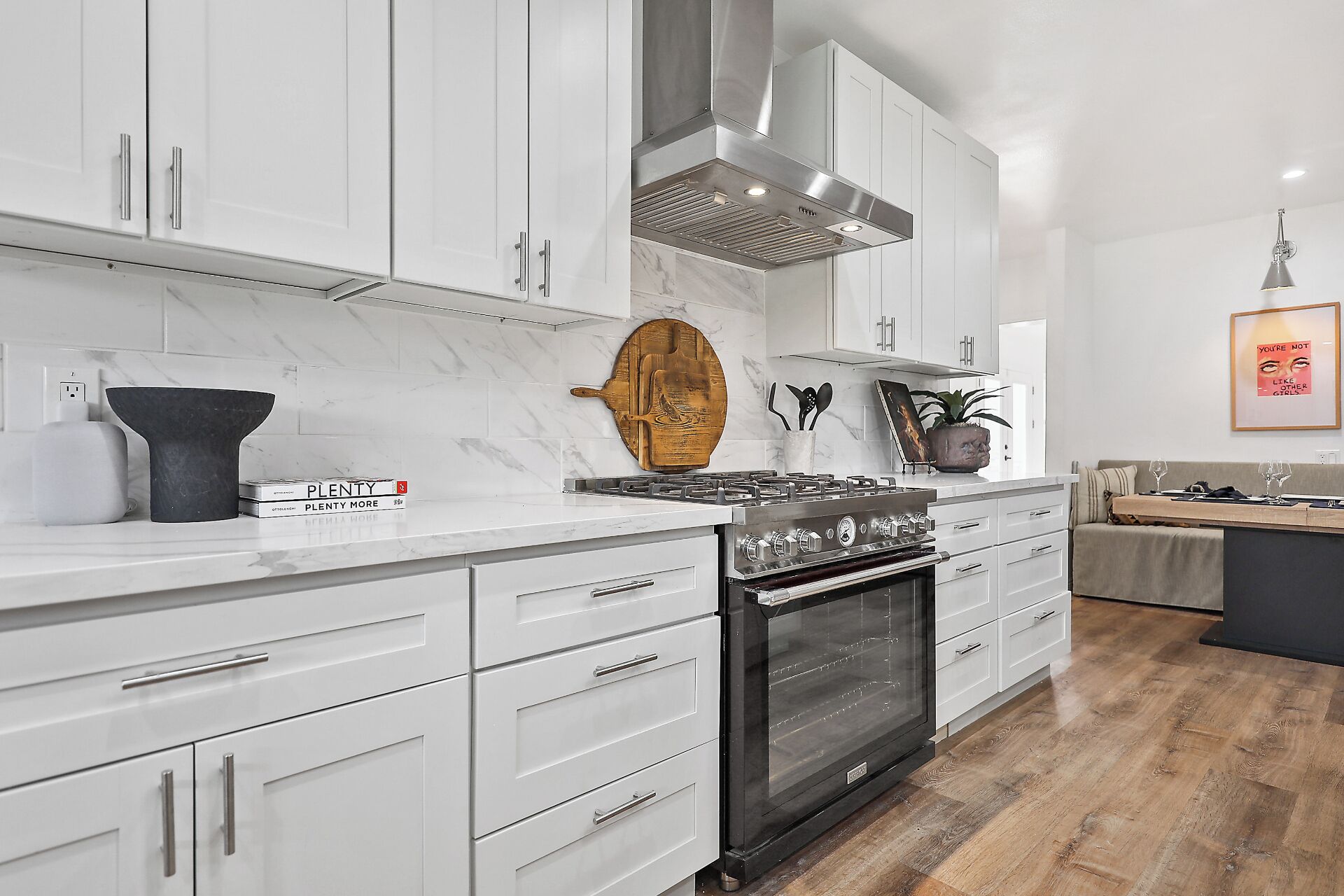 A modern kitchen with white cabinets, a stainless steel range hood, and a black oven.