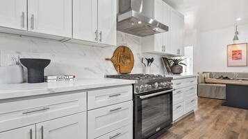 A modern kitchen with white cabinets, a stainless steel range hood, and a black oven.