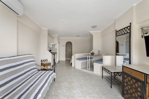 A hotel room with a bed, a small table, a bench, a mirror, and a kitchenette area. - Vacation Studio 'Santa María' with Sea View, Wi-Fi and Air Conditioning (Adeje)