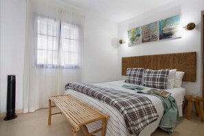 Une chambre à coucher comprenant un lit, un banc, une table de chevet, une lampe fixée au mur et des œuvres d’art.