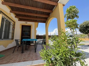 A patio with a table and chairs, a covered area with a wooden ceiling, and a view of a mountain in the background.