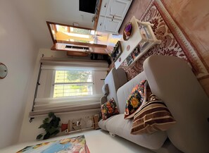 A cozy living room with a sofa, a small table, a TV, and a window with a view of greenery.