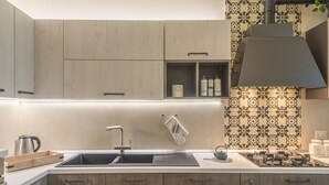 A modern kitchen with a built-in sink, wooden cabinets, a black range hood, and patterned backsplash tiles. - Casa Mabel - Lecce Selection (Lecce)