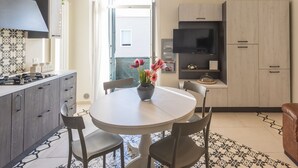 A modern kitchen with a round dining table, two chairs, a vase with flowers, and a view of the sea through an open door. - Casa Mabel - Lecce Selection (Lecce)