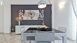 A modern dining area with a black table, white chairs, and a large abstract painting on the wall.