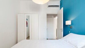 A bedroom with a bed, a wardrobe, a door leading to a bathroom, and a wall-mounted lamp.