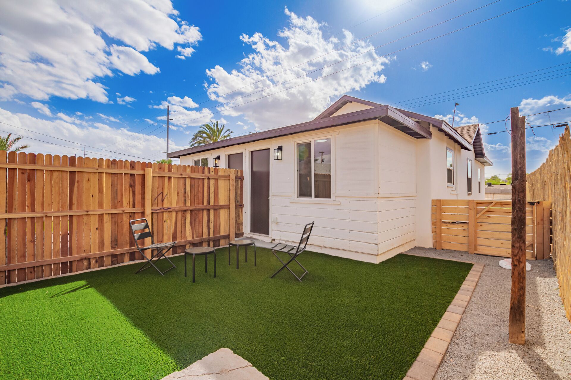 Une maison de plain-pied avec un jardin clôturé, une petite terrasse avec deux chaises et une pelouse bien entretenue.