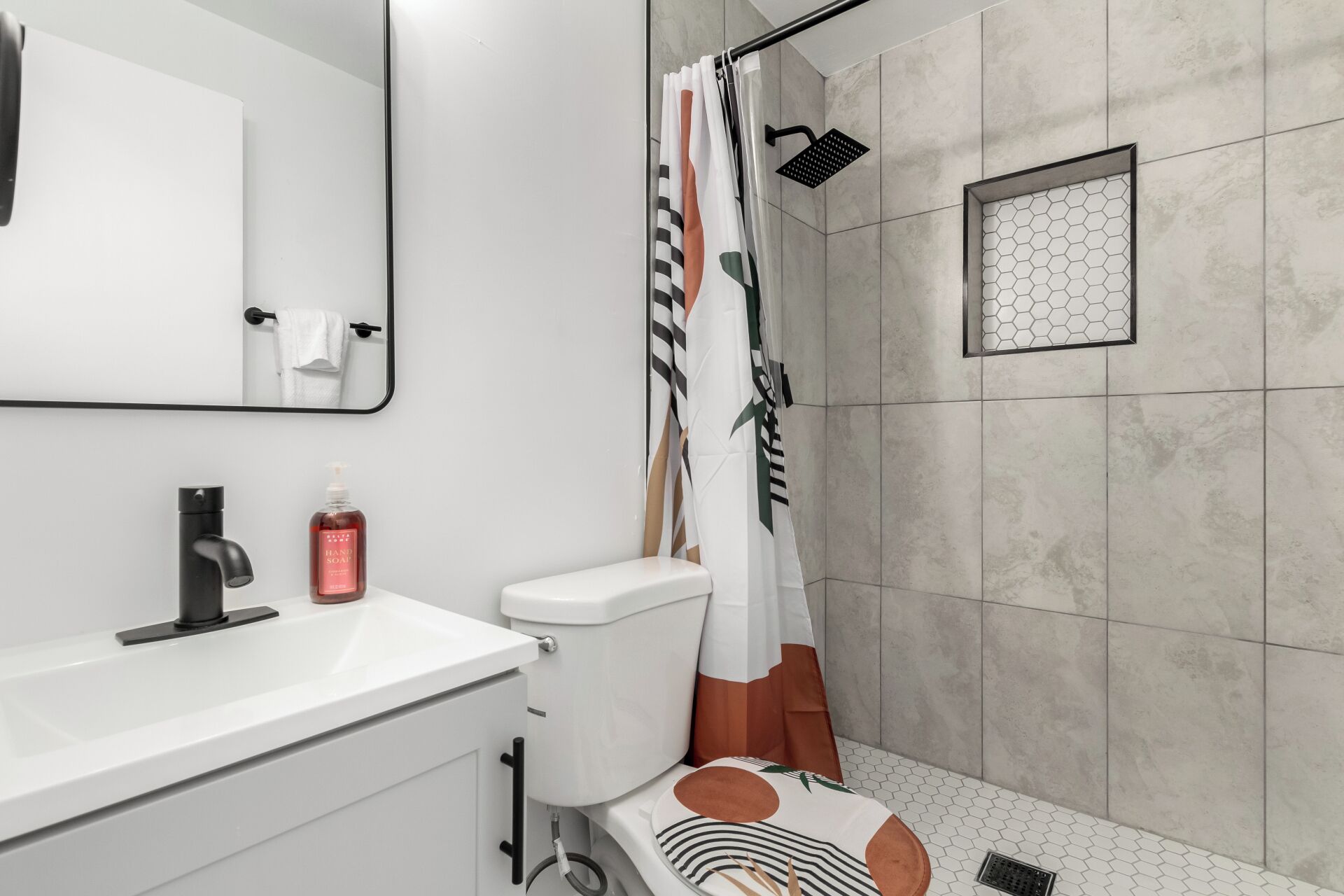 A modern bathroom with a white sink, a toilet, a shower with a geometric-patterned showerhead, and a mirror above the sink.