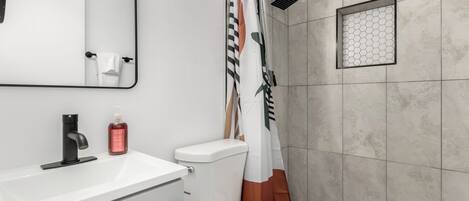A modern bathroom with a white sink, a toilet, a shower with a geometric-patterned showerhead, and a mirror above the sink.