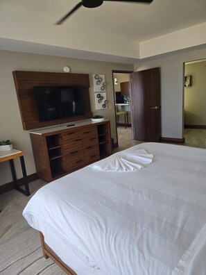 Un dormitorio con una cama grande, un televisor montado en un mueble de madera, una mesita con una planta y una puerta que da a un baño.