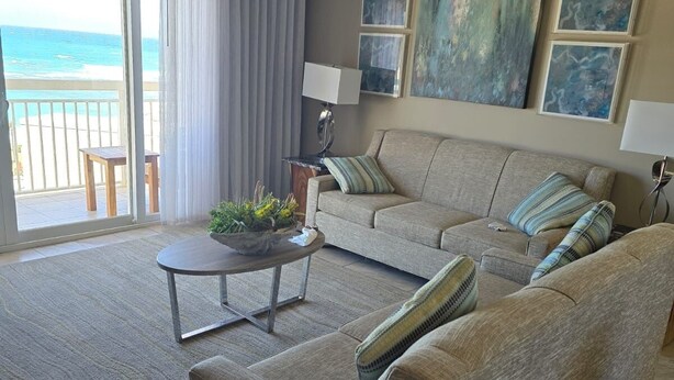 Ein geräumiges Wohnzimmer mit einer großen Couch, einem Couchtisch und Meerblick durch eine Schiebetür.