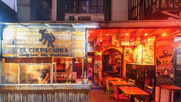 Une façade en bois d’un restaurant appelé « El Chupacabra », avec une enseigne indiquant qu’il sert de la bière bon marché, des plats de barbecue et des tacos de rue.
