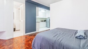 Une chambre avec un lit, un plancher en bois, une salle de bain avec douche et un coin cuisine.