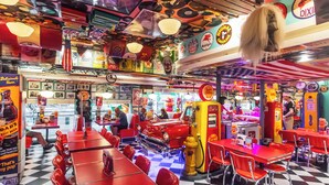 Un restaurant avec des banquettes et des tables rouges, une voiture ancienne et divers jeux d’arcade.