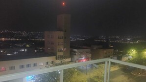 Vista nocturna desde un balcón con vistas a un paisaje urbano de edificios y una ciudad distante.