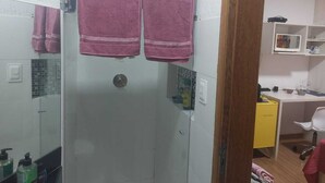 Un baño con cabina de ducha de vidrio, dos toallas rosas colgadas de ganchos y un armario amarillo.