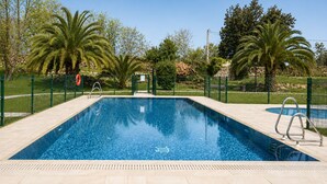 A rectangular swimming pool with clear blue water, surrounded by a stone-tiled deck, a metal ladder, and a green fence. - Tejasturias : La Franca Swimming Pool, Paddle Tennis and Beach (Noriega)