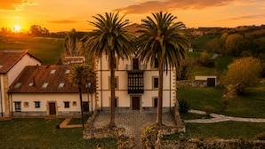 A traditional building with a central staircase, palm trees, and a surrounding garden. - Tejasturias : La Franca Swimming Pool, Paddle Tennis and Beach (Noriega)