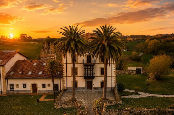A traditional building with a central staircase, palm trees, and a surrounding garden.