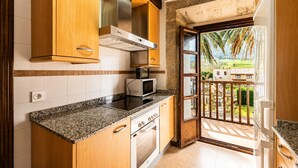 A kitchen with wooden cabinets, a microwave, and a view of a balcony with a house and palm trees. - Tejasturias : La Franca Swimming Pool, Paddle Tennis and Beach (Noriega)