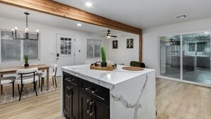 A modern kitchen with a marble island, wooden ceiling beams, and a sliding glass door leading to a balcony. - Charming 3-bedroom house in welcoming Downtown Gilbert with WiFi, AC (Gilbert)