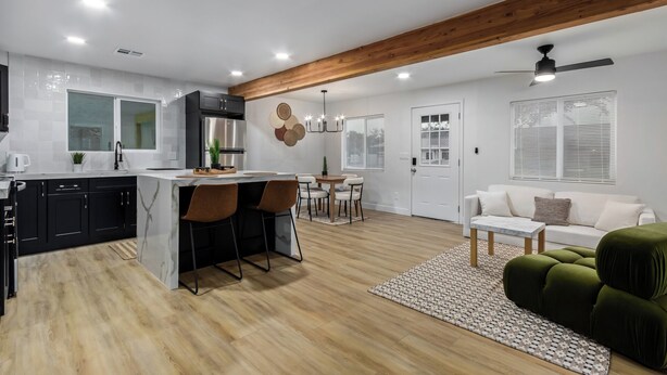 A modern kitchen with a central island, black cabinets, and a stainless steel refrigerator. There is a dining area with a wooden table and chairs, and a living room with a green sofa and a white couch. - Charming 3-bedroom house in welcoming Downtown Gilbert with WiFi, AC (Gilbert)