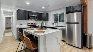 A modern kitchen with dark cabinets, stainless steel appliances, and a marble island with seating. - Charming 3-bedroom house in welcoming Downtown Gilbert with WiFi, AC (Gilbert)