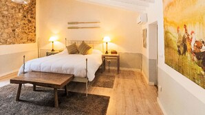 A bedroom with a bed, bedside tables, a bench, a stone wall, and a painting.