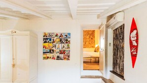 A hallway with a white wardrobe, a wall collage of photos, a bed in the background, and a red surfboard decoration.