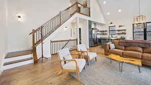 A spacious living room with a wooden staircase, a brown leather sofa, and a dining area.