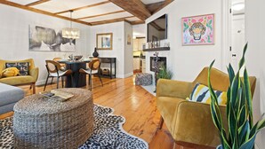 A spacious living area with wooden beams, a dining set, and a kitchen in the background.