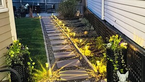 A stone pathway leading to a house with a small garden area and a statue.