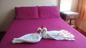A bed with a purple bedspread and two white towels arranged in swan shapes.