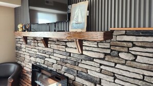 A stone wall with a fireplace, a wooden shelf with a painting, and a television mounted on the wall. - Ocean Pearl-Beach block, Quick stroll to Boardwalk (Atlantic City)