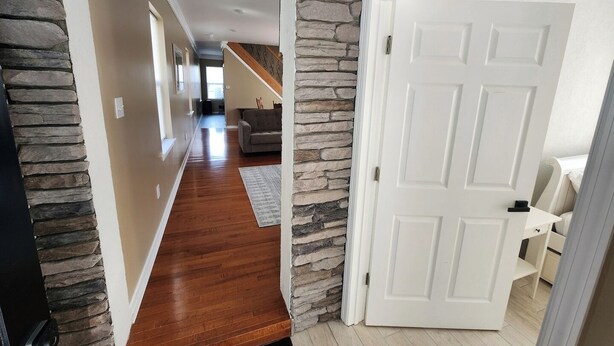 A hallway with a stone accent wall, wooden flooring, and a white door leading to a room. - Ocean Pearl-Beach block, Quick stroll to Boardwalk (Atlantic City)