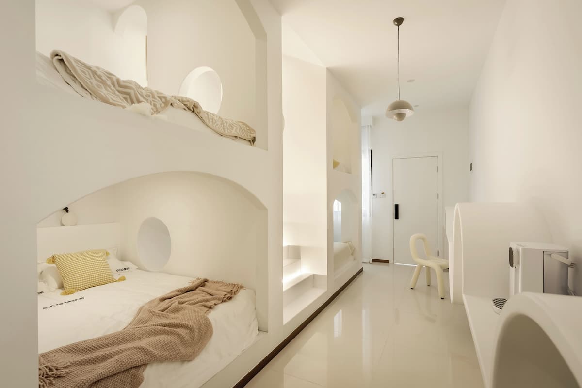 Quarto de hotel moderno com beliche, mesa de cabeceira, cadeira e pequena escrivaninha.