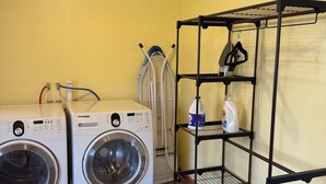 Une buanderie équipée de deux machines à laver à chargement frontal, d’un étendoir et d’une étagère métallique contenant des produits de lessive.