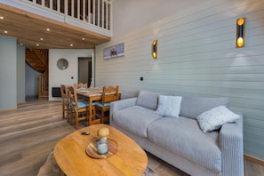 A modern living room with a wooden dining table, a sofa, and a ceiling with exposed beams.